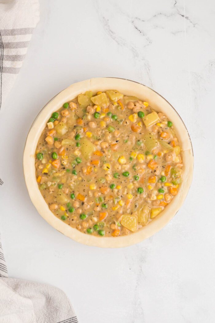 An unbaked pot pie without the crust so you can see the filling mixture made from potato, chickpeas, carrot, corn, peas and potato.