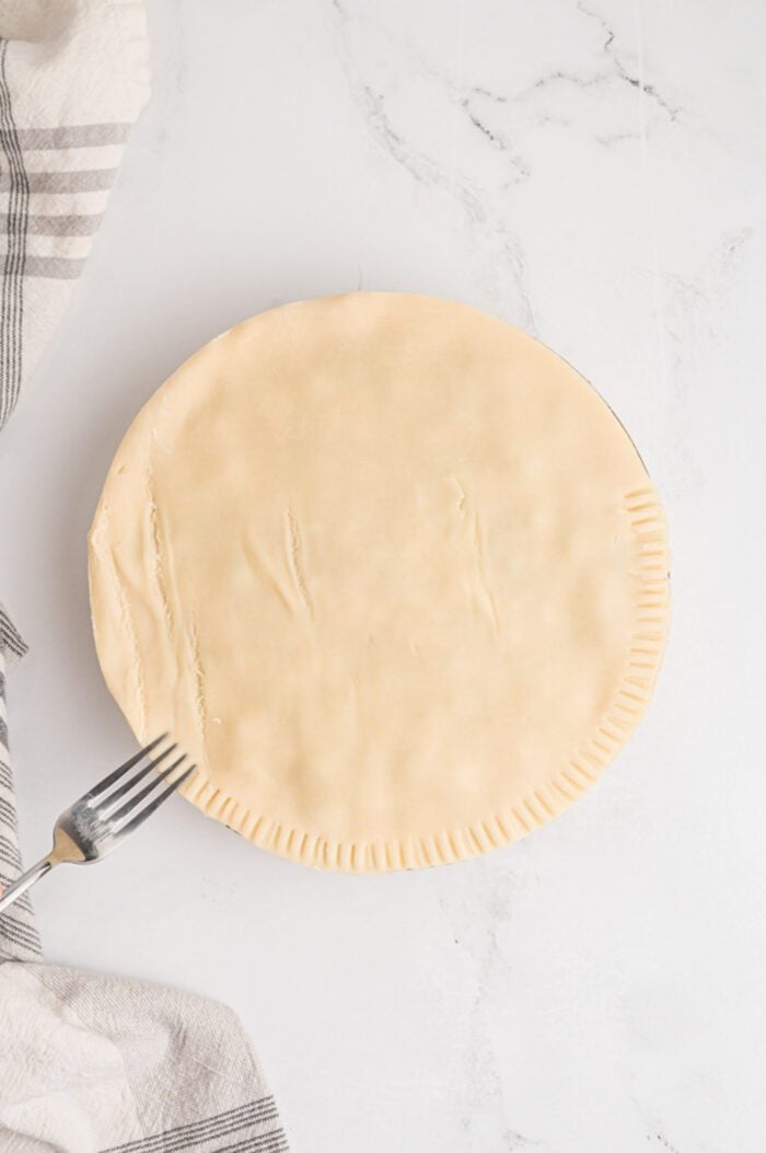 A fork pressing around the edge of a pie to form a textured look to the edge of the crust.