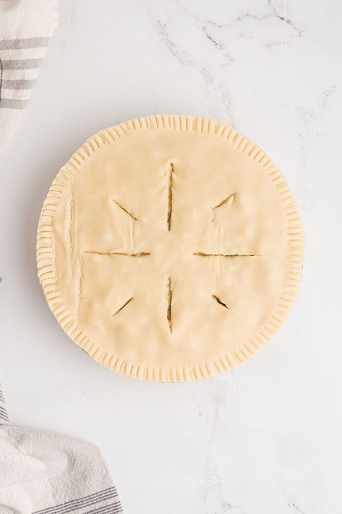 The top of an unbaked pie with 8 small slits in the top forming a pretty pattern.