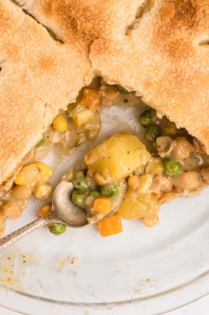 Overhead view into a pie dish of veggie pot pie with a slice taken from it. There is a spoon resting in the dish with some of the vegetable filling on it.