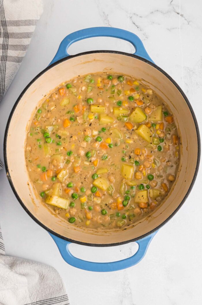 A thick pot pie filling mixture made from potatoes, chickpeas, peas, corn and carrot cooking in a large soup pot with handles.