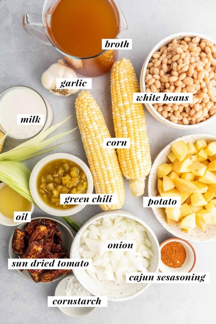 All ingredients needed for making a summer corn chowder recipe with sun dried tomato, green chili and white beans. Each ingredient is labelled with text and the list can be found on the page in the recipe card..