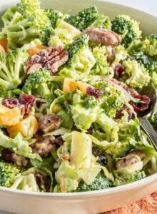 Broccoli apple salad with cranberries, pecans and brussels sprouts in a salad bowl with a spoon.