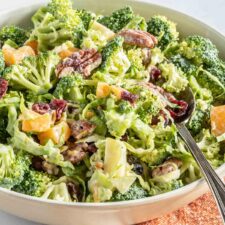 Broccoli apple salad with cranberries, pecans and brussels sprouts in a salad bowl with a spoon.