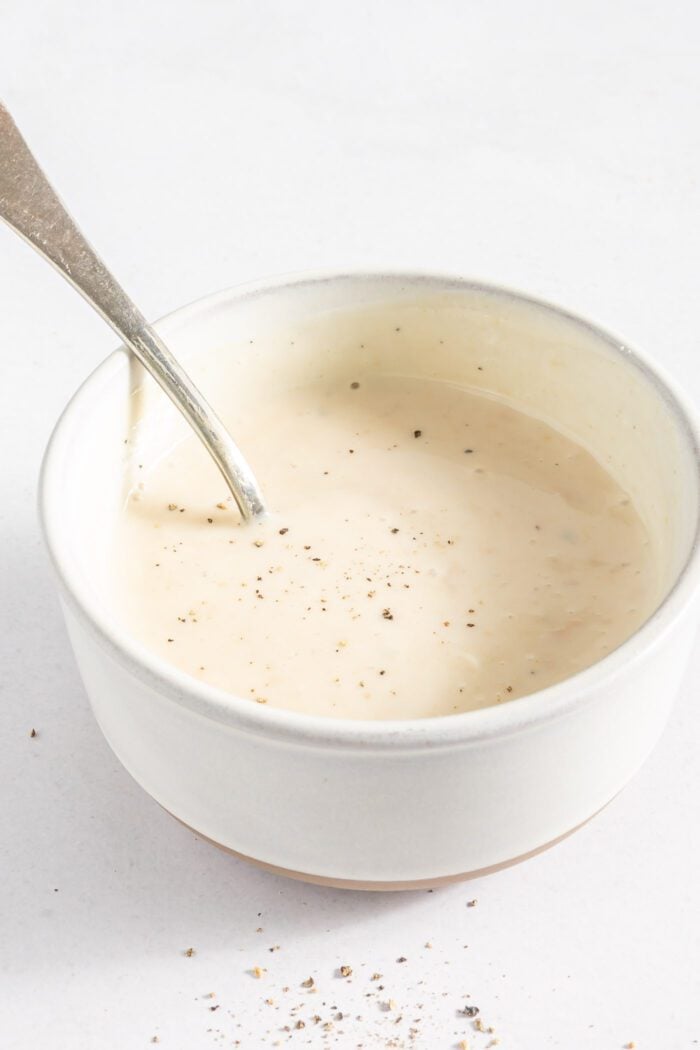 Creamy mayo-based dressing for broccoli salad mixed up in a small bowl with a spoon.