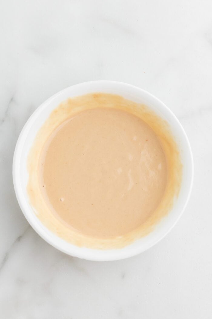 Creamy tahini dressing mixed up in a small white bowl on a marble surface.