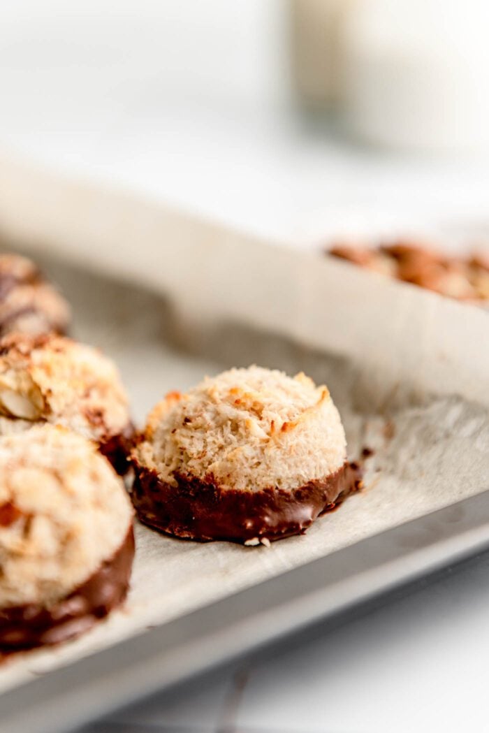 A small almond macaroon dipped in chocolate on a baking tray lined with parchment paper.