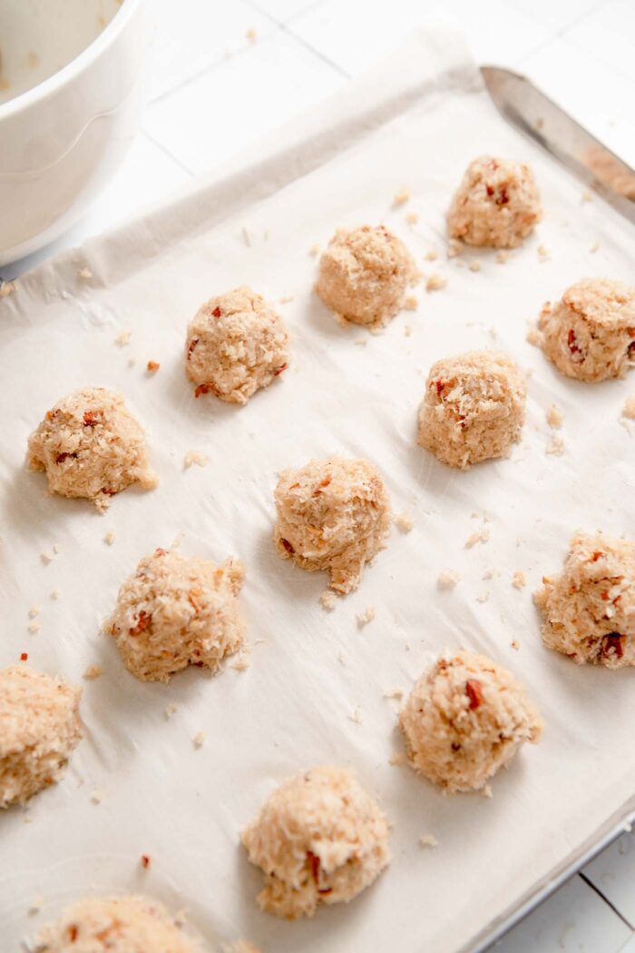15 small unbaked almond coconut macaroons on a baking tray lined with parchment paper.