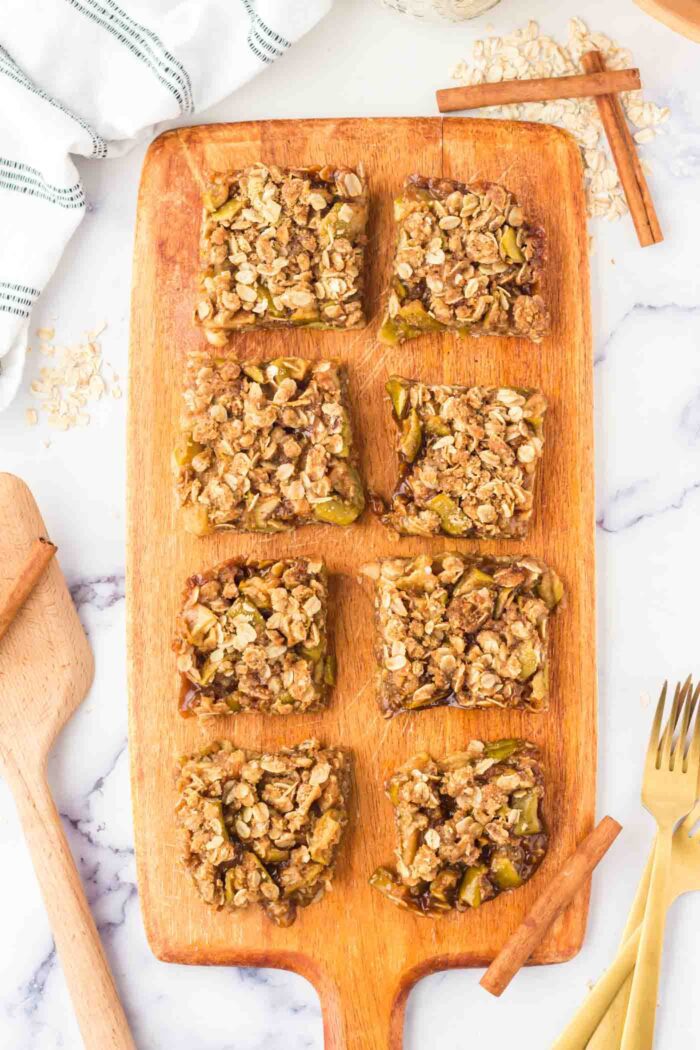 8 square portions of apple crumble bars on a rectangular cutting board with a handle.