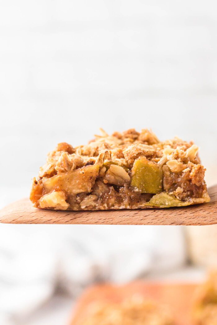 An apple pie crumble bar held on a a wooden spatula.