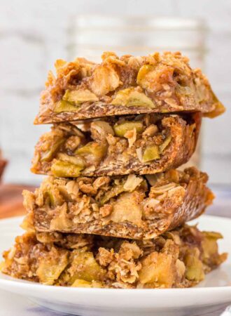 Stack of 4 apple crumble bars on a plate. The bars have an oatmeal crust and crumble topping with a layer of apple pie filling in between.