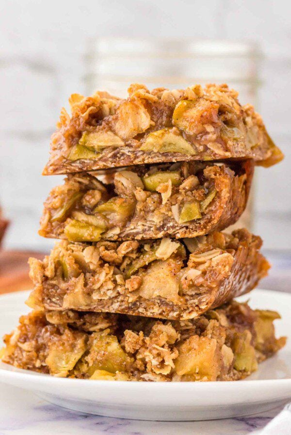 Stack of 4 apple crumble bars on a plate. The bars have an oatmeal crust and crumble topping with a layer of apple pie filling in between.