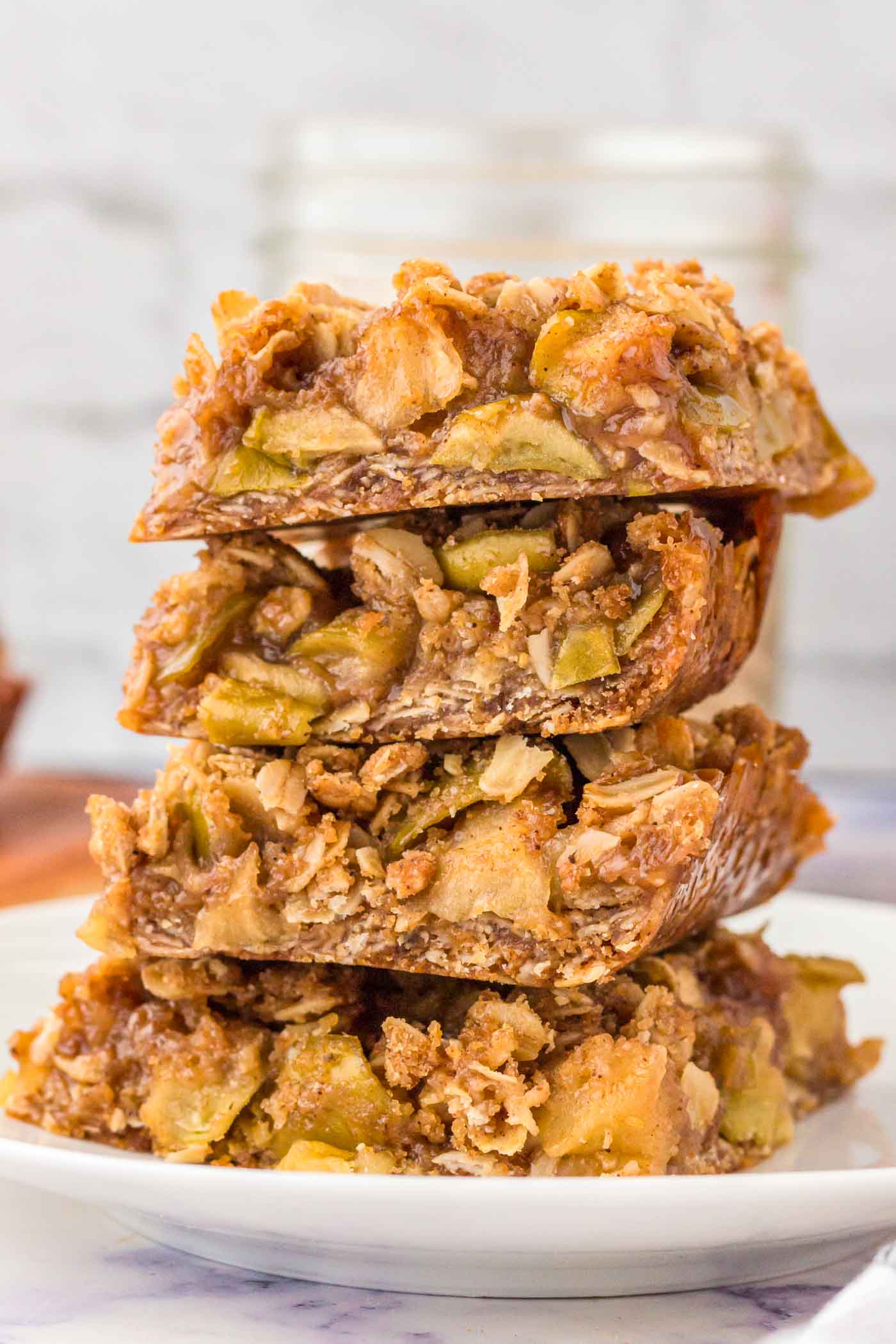 Stack of 4 apple crumble bars on a plate. The bars have an oatmeal crust and crumble topping with a layer of apple pie filling in between.