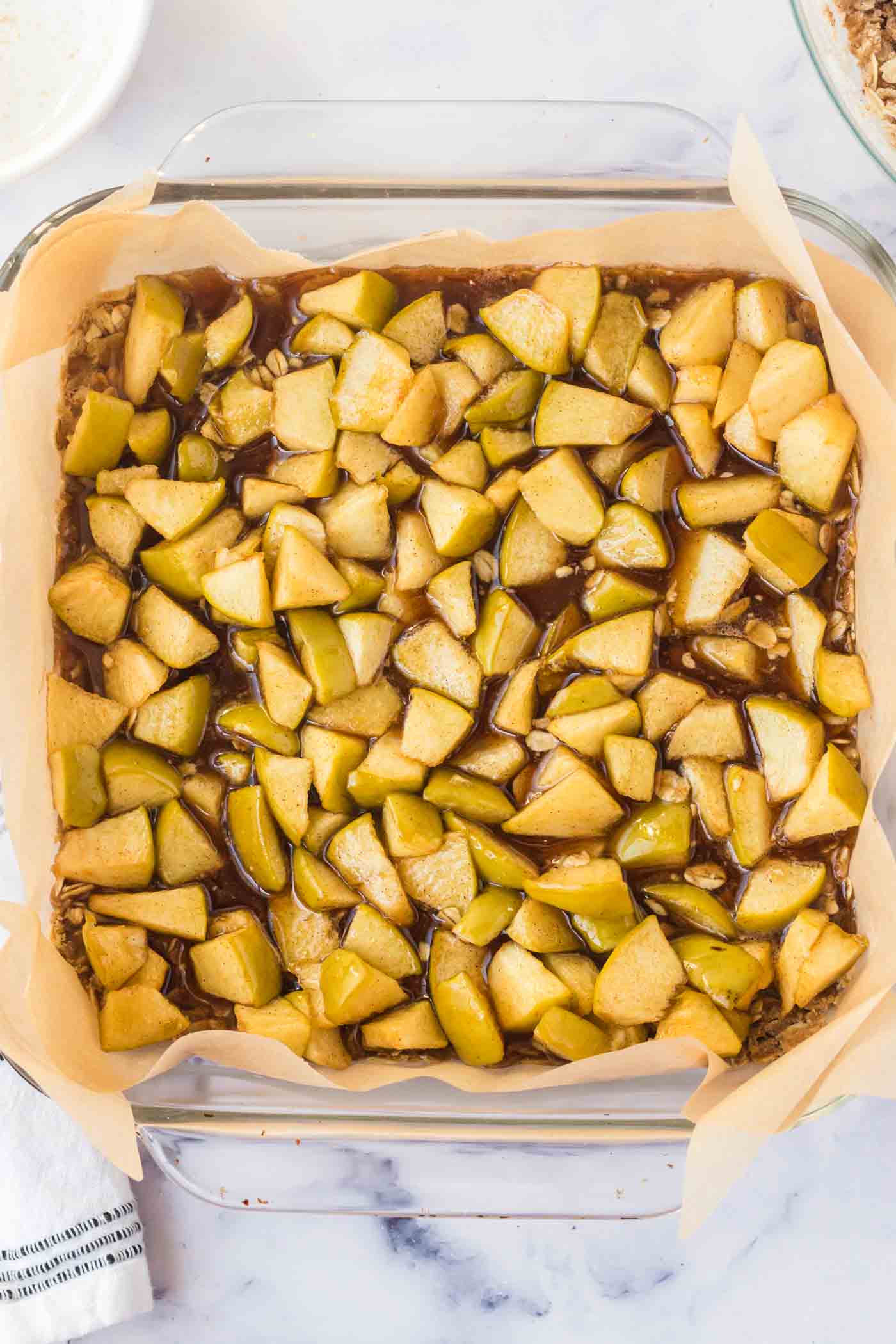 Overhead view into a square glass baking dish filled with diced apples and lined with parchment paper.