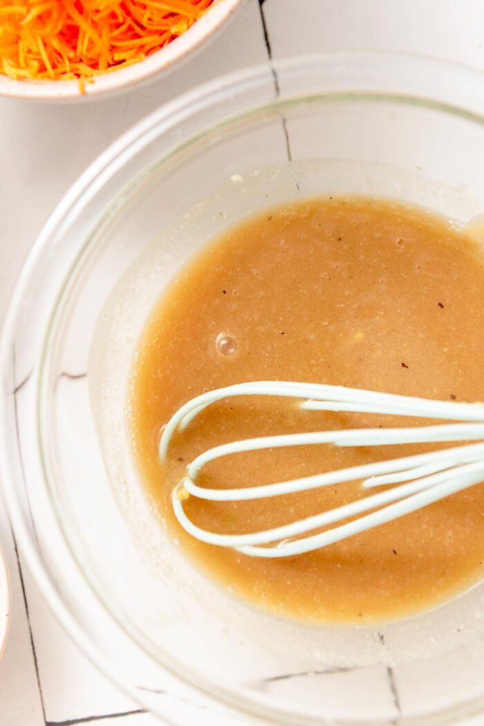 Sesame salad dressing mixed up in a small glass bowl with a whisk.