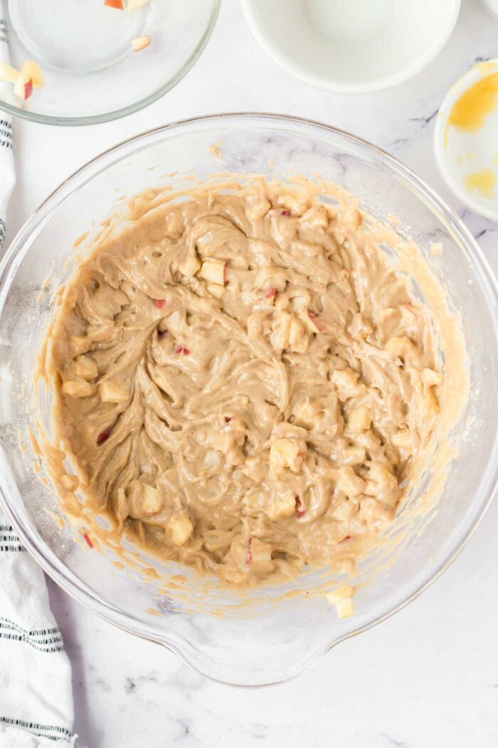 Raw apple cake batter with pieces of diced apple in a large glass mixing bowl.