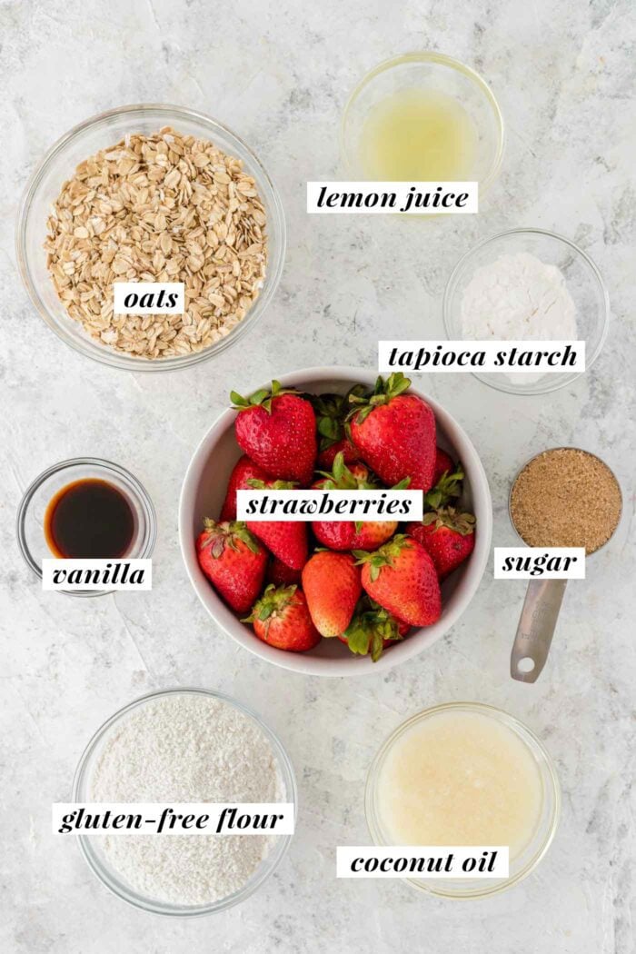 Strawberry oatmeal bar ingredients gathered in bowls on a countertop. Each ingredient is labelled with text overlay. The ingredient list can be found on the corresponding blog page.