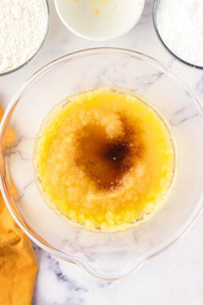 Vanilla and applesauce with creamed oil and sugar in a large glass mixing bowl on a marble countertop.