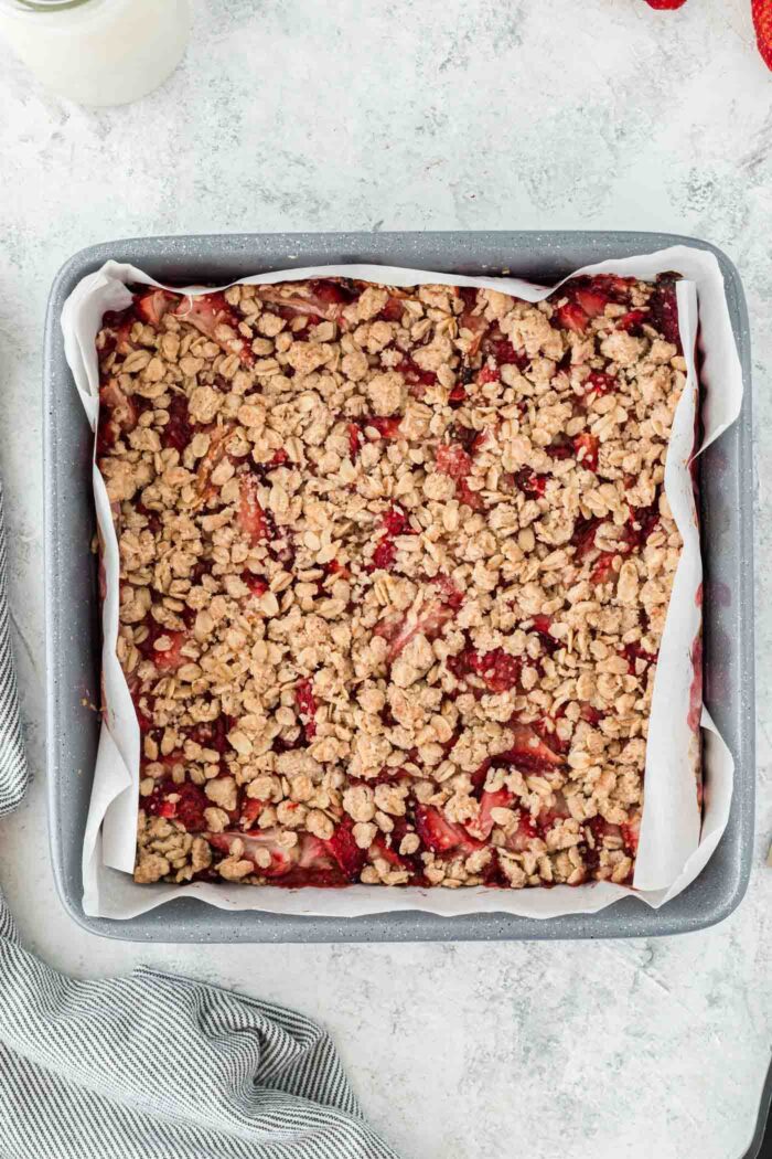 Overhead view of a square baking pan of strawberry oat bars. The pan is lined with parchment paper.