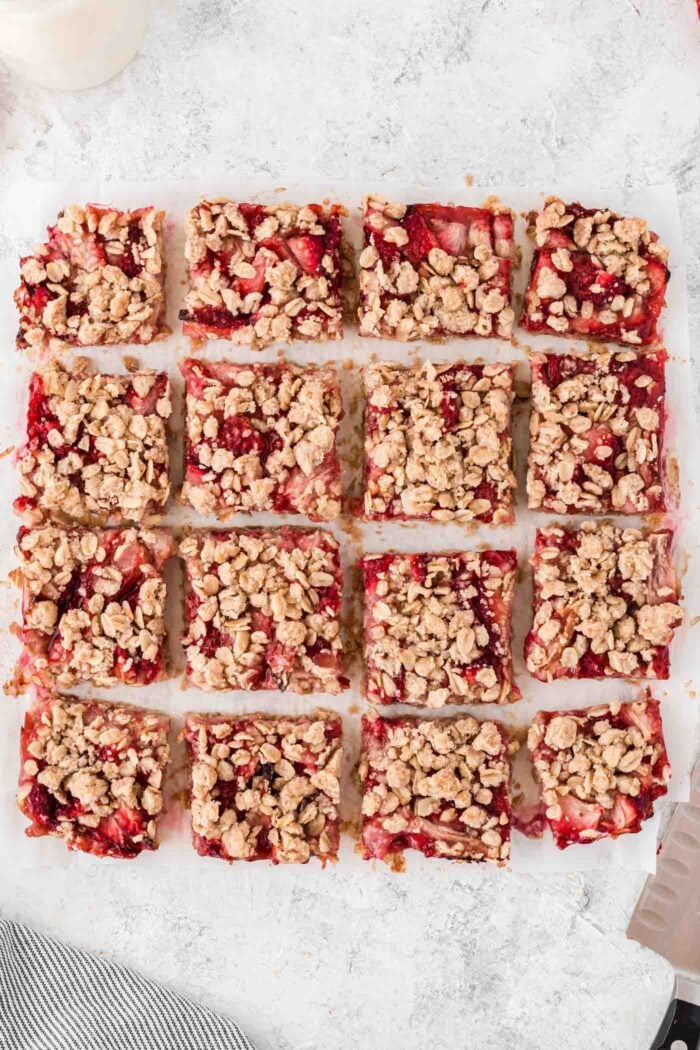 Strawberry oatmeal bars cut into 16 even squares on a piece of parchment paper. A knife rests beside the bars.