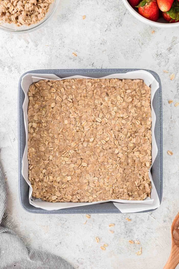 A layer of oatmeal crust pressed into a square baking pan lined with parchment paper.