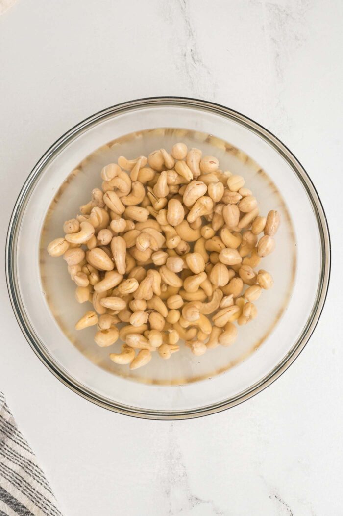 Raw cashews soaking in water a glass bowl.