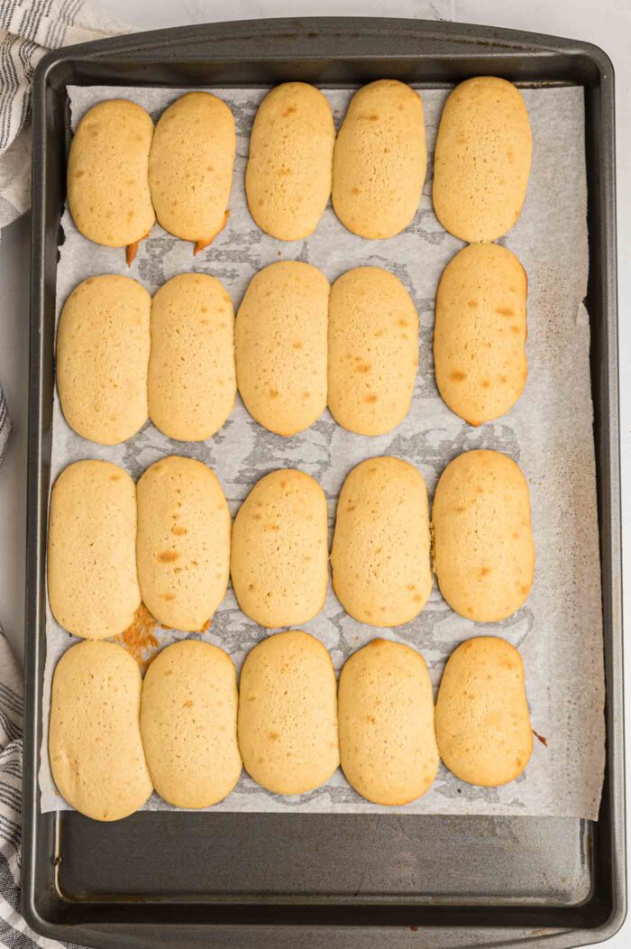 20 homemade baked ladyfingers on a baking tray lined with parchment paper.