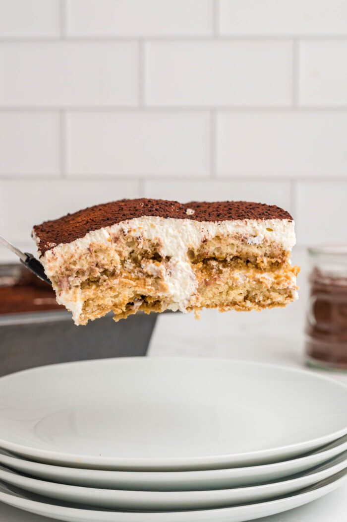 A square of tiramisu on a spatula being transferred from a pan to a small serving plate.