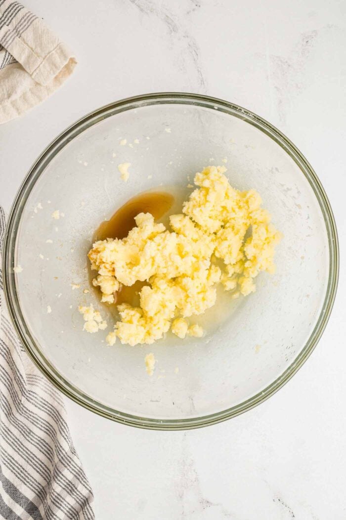 A chunky butter mixture in a glass mixing bowl with some vanilla.