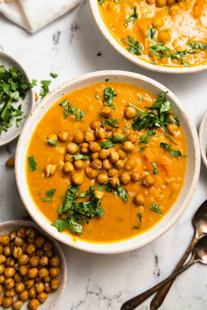 Overhead view of a creamy sweet potato lentil soup topped with crispy chickpeas and a sprinkle of chopped fresh cilantro.