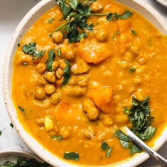 Overhead view of a creamy sweet potato carrot lentil soup topped with crispy chickpeas and a sprinkle of chopped cilantro.