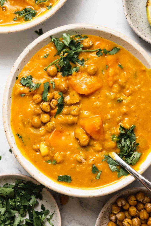 Overhead view of a creamy sweet potato carrot lentil soup topped with crispy chickpeas and a sprinkle of chopped cilantro.