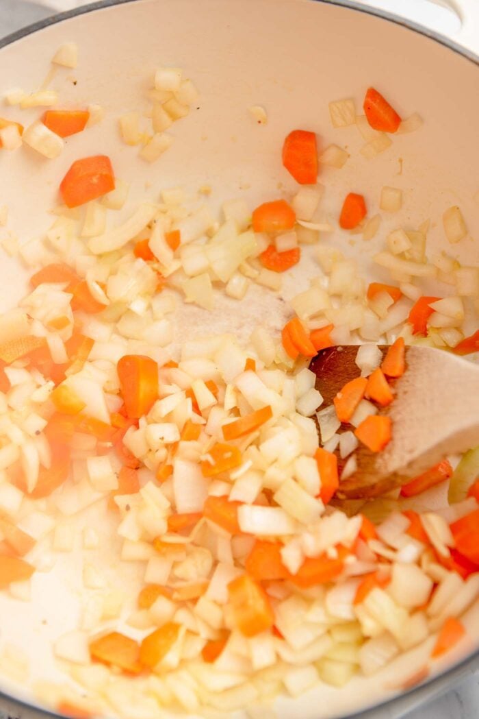 Chopped onion, garlic, ginger and carrot cooking in a large soup pot with a wooden spoon.