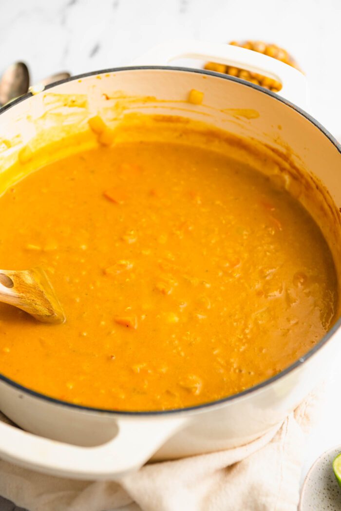 Creamy soup made with sweet potato and red lentils cooking in a pot with a wooden spoon.