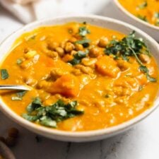 A bowl of sweet potato lentil soup topped with crispy chickpeas and cilantro. A second bowl can be seen in the background.