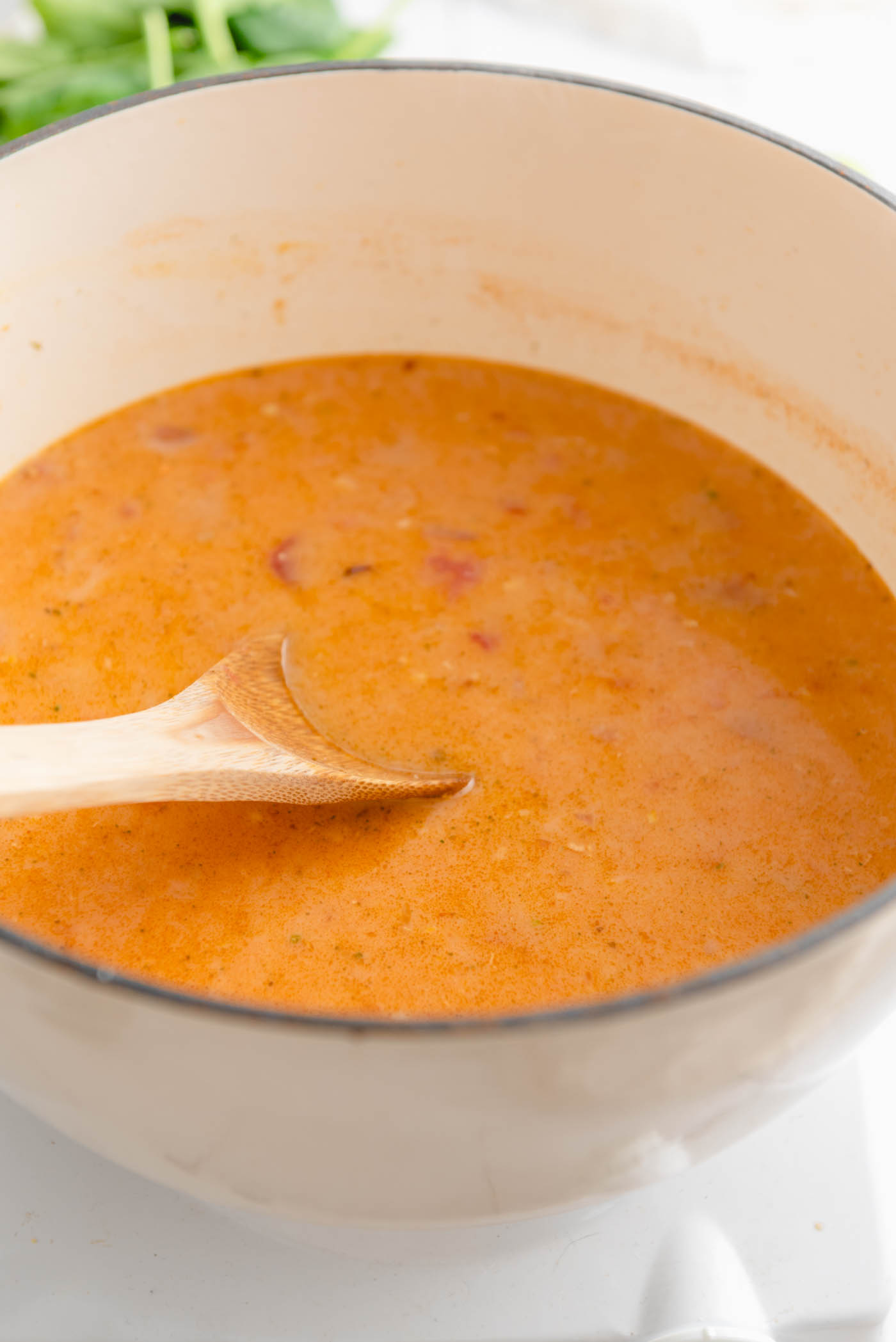 A creamy red curry cooking in a large Dutch oven with a wooden spoon.