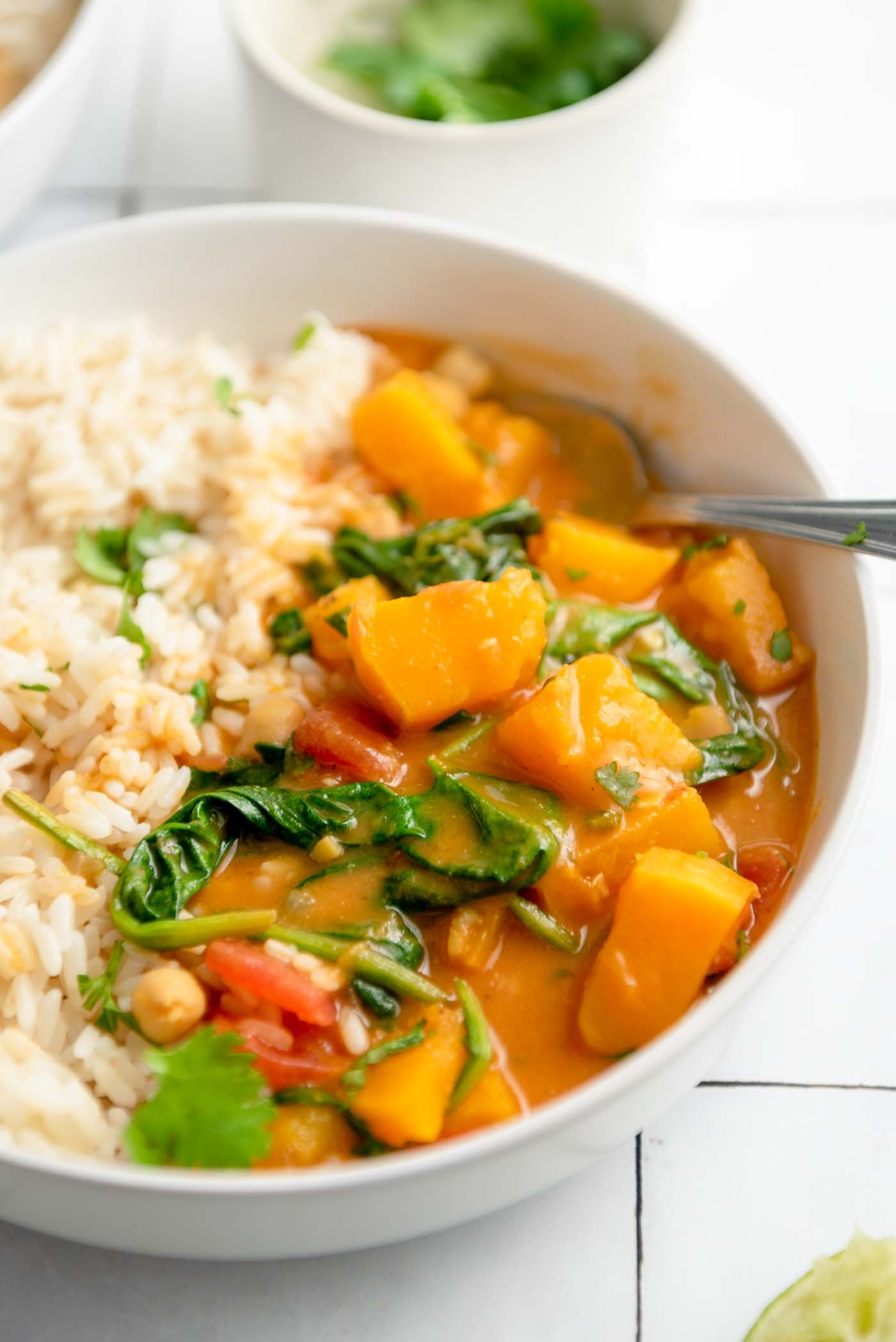 A bowl of roasted butternut squash curry with spinach and chickpeas served with rice.