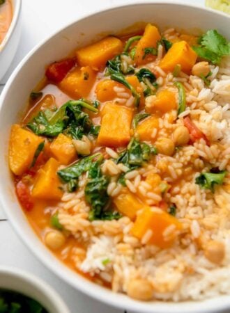 A bowl of roasted butternut squash curry with spinach and chickpeas served with rice and topped with chopped cilantro.