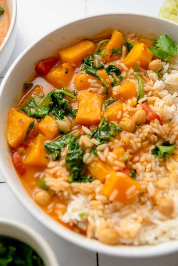 A bowl of roasted butternut squash curry with spinach and chickpeas served with rice and topped with chopped cilantro.