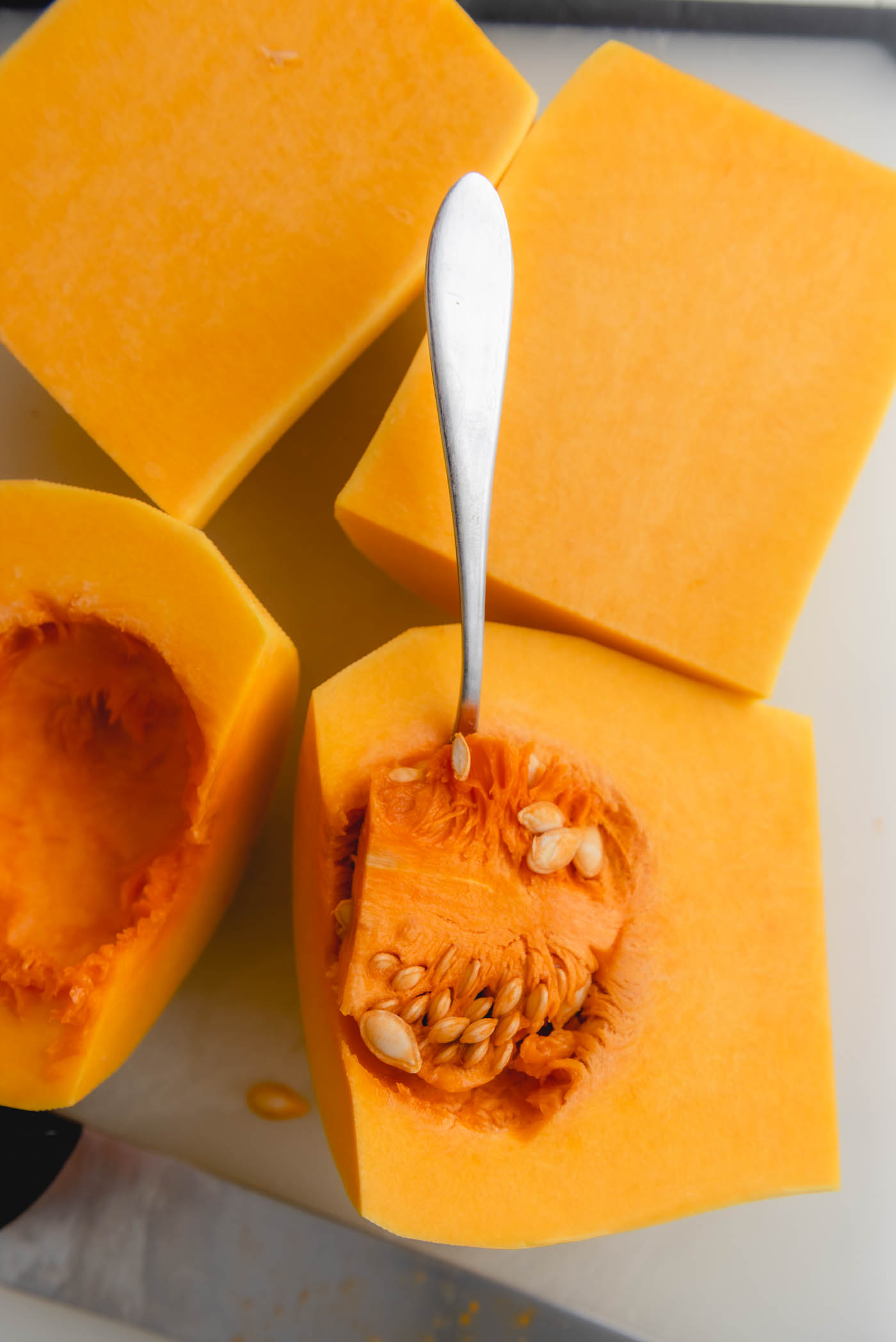 A spoon scooping the seeds out of a peeled butternut squash half.