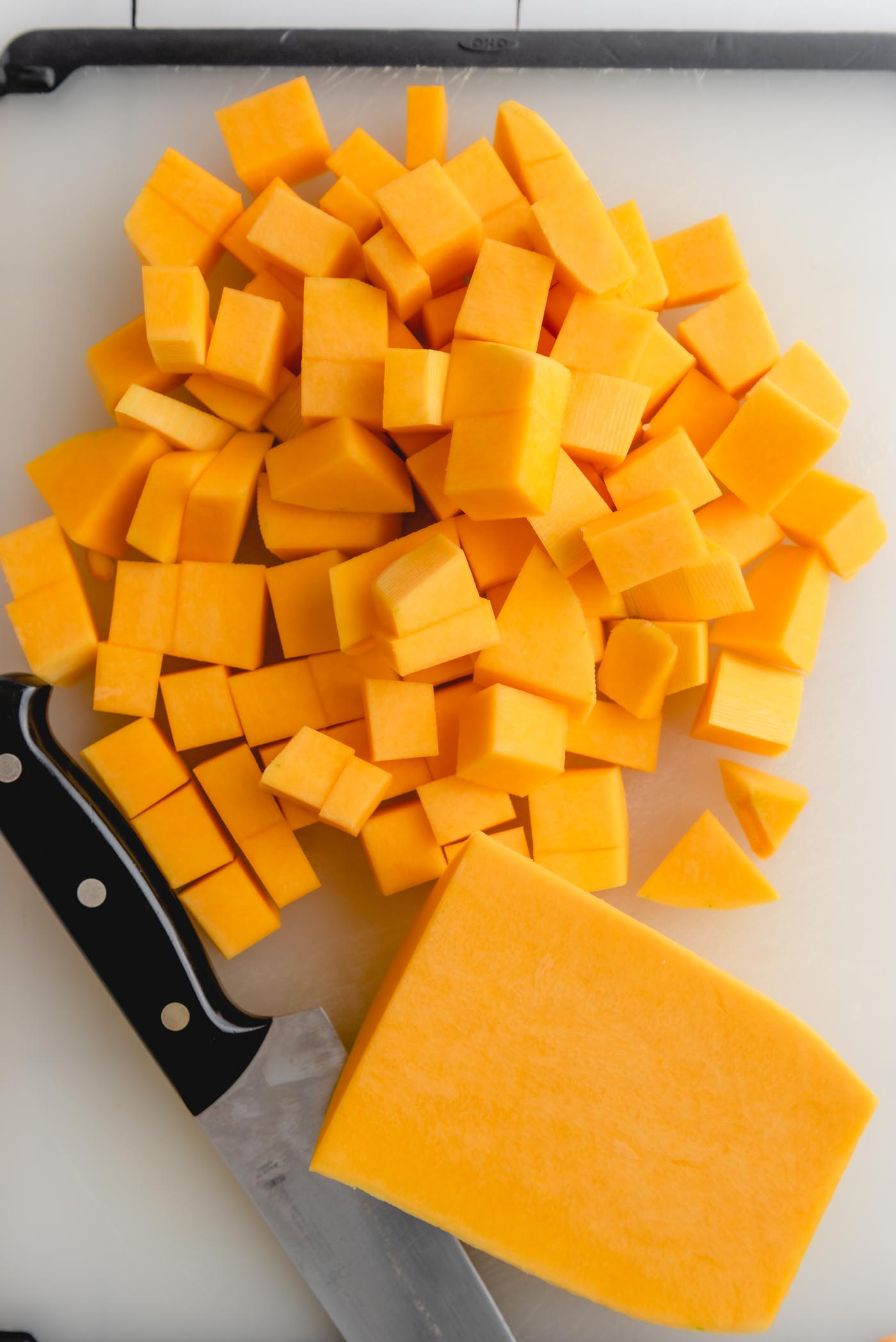 Cubed butternut squash in a pile on a cutting board with a knife beside it.