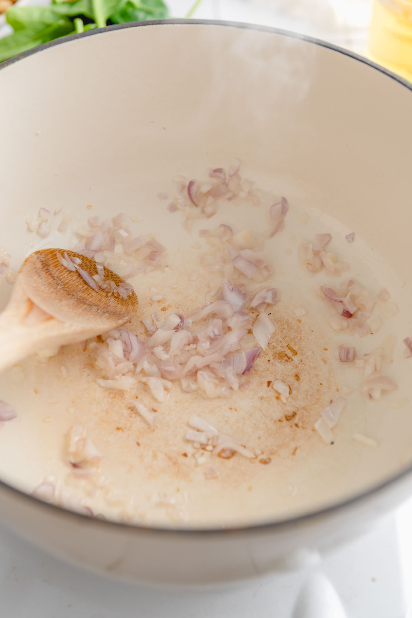 Minced shallot cooking in a large soup pot with a wooden spoon.