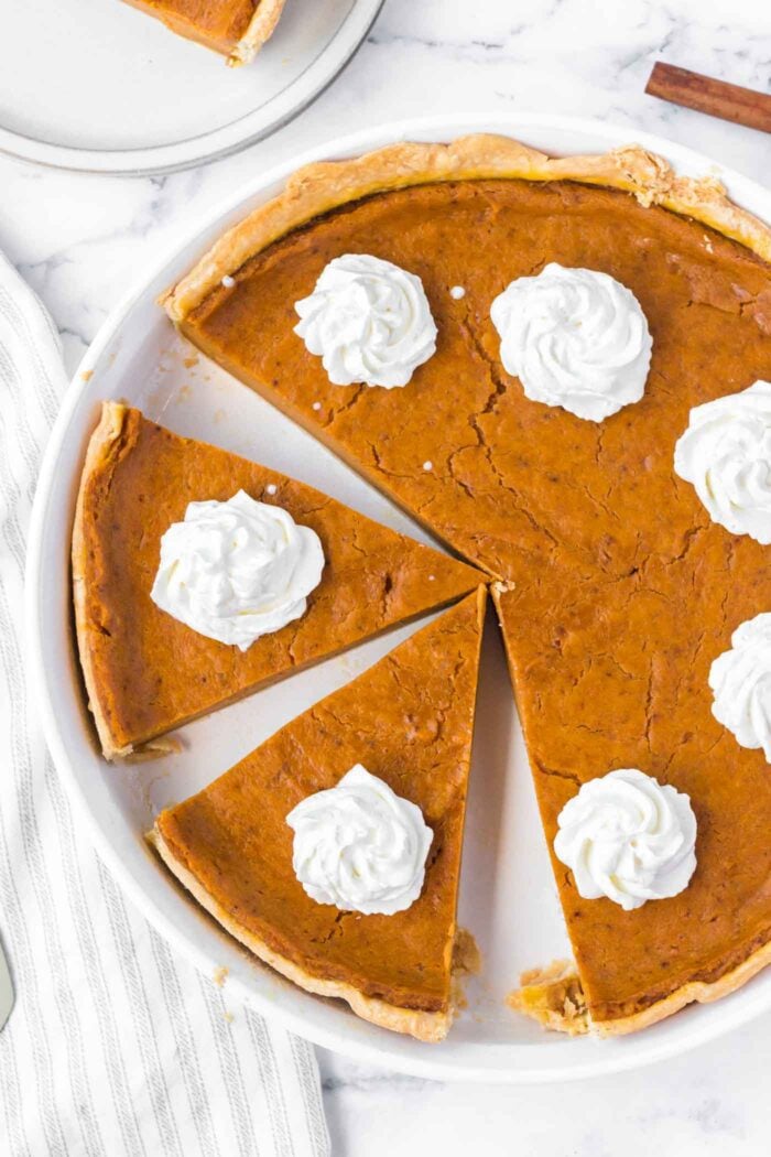 Overhead view of a vegan sweet potato pie cut into slices and topped with dollops of whipped cream.