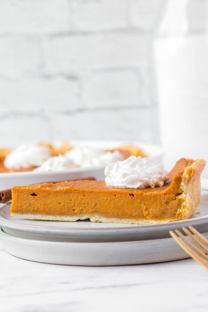 A slice of sweet potato pie topped with a dollop of whipped cream on a plate.