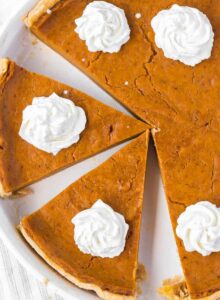 Overhead view of a vegan sweet potato pie cut into slices and topped with dollops of whipped cream.