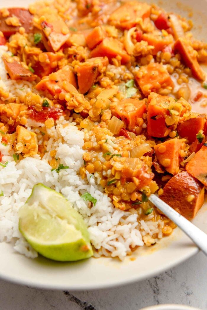 Close up of a bowl of sweet potato lentil curry with rice and a wedge of lime.