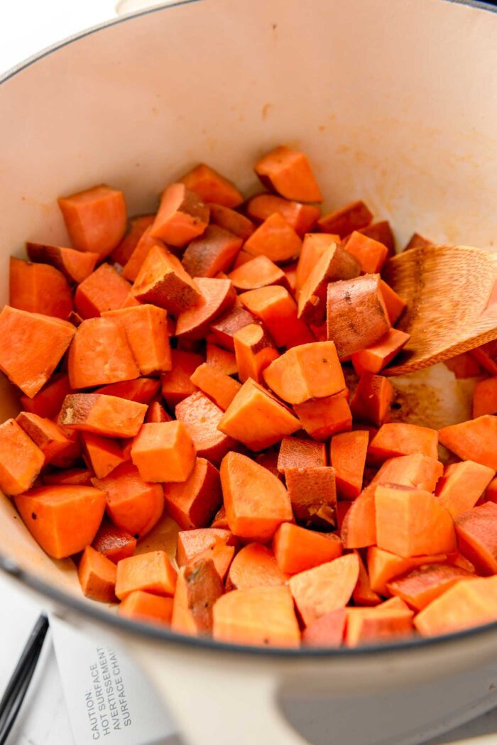 Cubes of sweet potato cooking in a large pot with a wooden spoon in it.