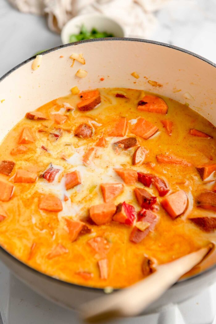 Coconut milk, diced tomato, sweet potato and broth cooking in a large pot on the stovetop.