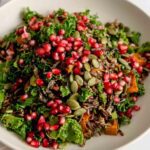 A bowl of colourful wild rice salad topped with pomegranate arils and pumpkin seeds.