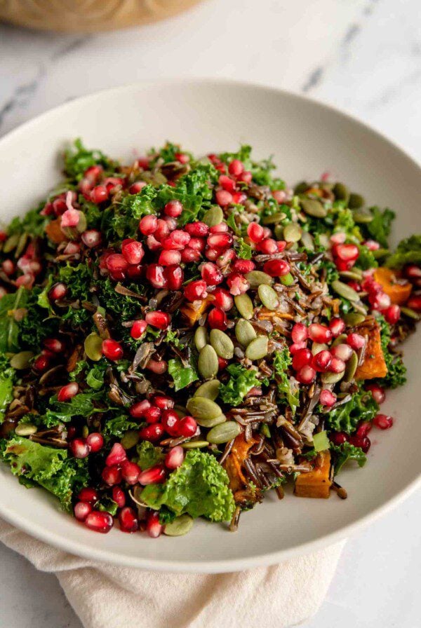 A bowl of colourful wild rice salad topped with pomegranate arils and pumpkin seeds.